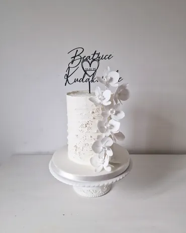 Single-tier white textured wedding cake with cascading white orchids and personalised topper