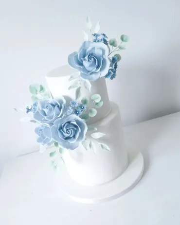 Two-tier white wedding cake with dusty blue sugar roses and leaves