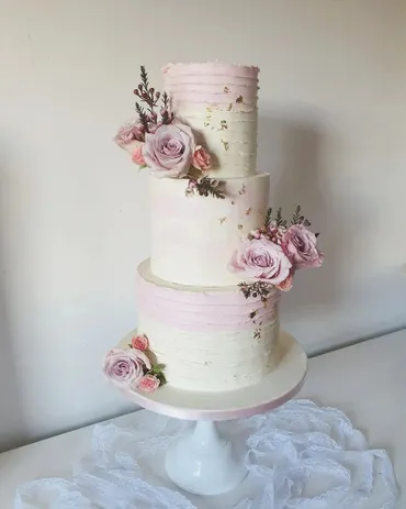 Three-tier white wedding cake with blush pink brushstroke texture and mauve roses