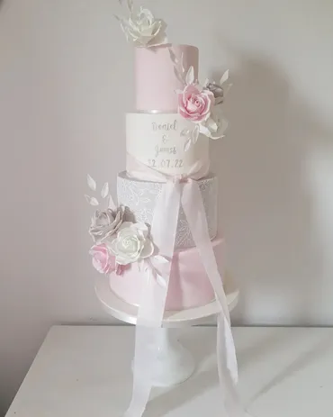 Four-tier white wedding cake with white roses and greenery on a wooden log stand in a barn venue