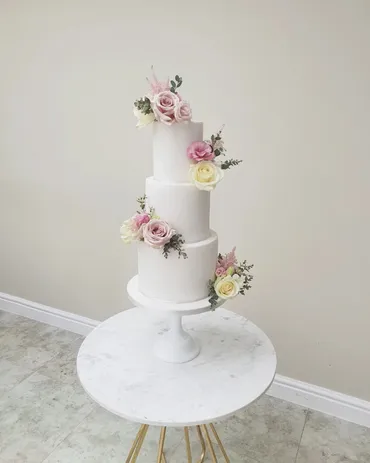 Three-tier white wedding cake with cascading pink and mauve roses and Mr & Mrs Kenworth topper