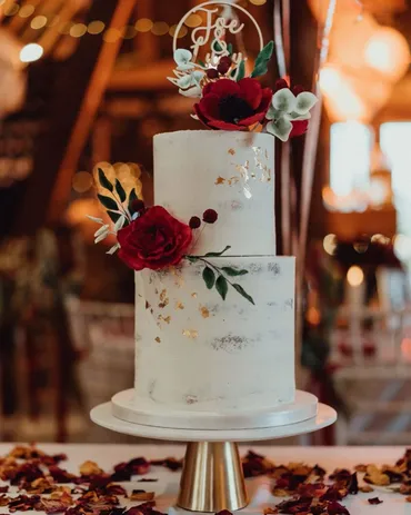 Three-tier white wedding cake with taupe sugar roses and gold monogram K & J initials