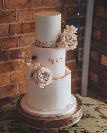 Two-tier semi-naked wedding cake with deep red anemones and gold leaf detail in a barn venue