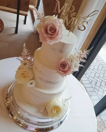 Three-tier white wedding cake with navy blue sugar flowers and gold calligraphy detail