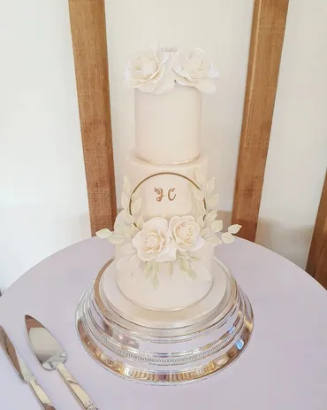 Three-tier navy blue wedding cake with pink ribbon and fresh pink roses and flowers