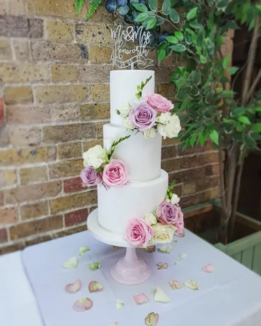 Four-tier white wedding cake with cascading pink and cream roses on a marble stand