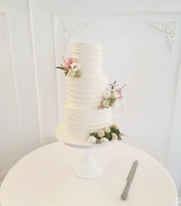 Two-tier semi-naked wedding cake with white roses and gold Mr & Mrs Chambers topper on a wooden log stand