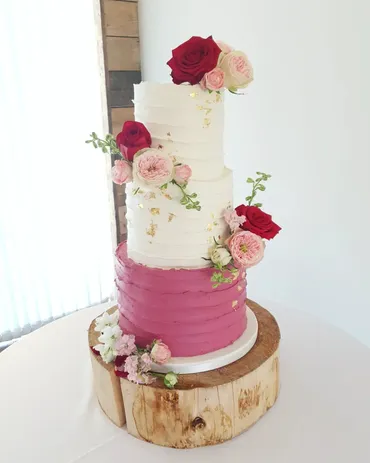 Three-tier white textured wedding cake with blush peonies and greenery in a barn venue