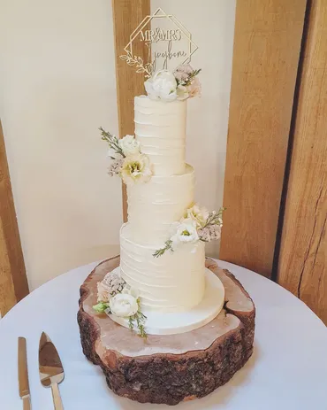 Three-tier white textured wedding cake with white roses and eucalyptus on a wooden log stand