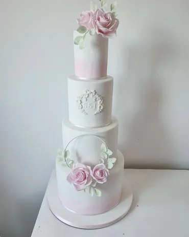 Close-up of white wedding cake tier with gold hoop, white sugar rose and sage green leaves