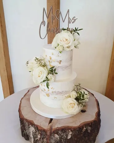 Three-tier white ruffled wedding cake with pink and white fresh flowers on a white cake stand