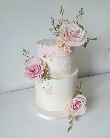 Two matching single-tier semi-naked wedding cakes with peach roses on wooden log stands