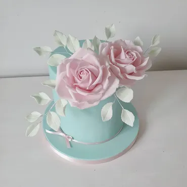 Three-tier white wedding cake with hand-painted tree and custom figurine topper on a wooden slice