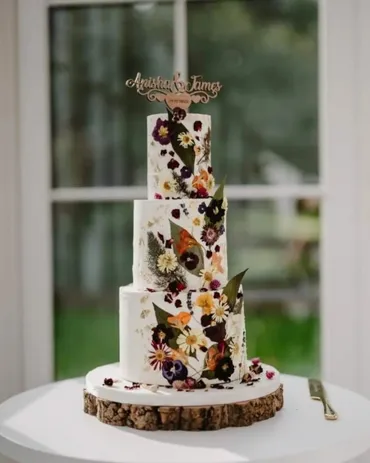 Four-tier white wedding cake with pressed flowers and Anishka & James topper