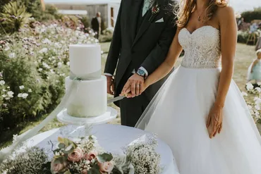 Five-tier white and gold glitter wedding cake with white flowers and greenery on a wooden log stand in a church venue with LOVE light-up letters