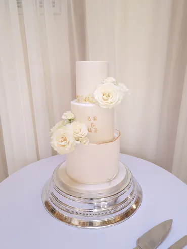 Three-tier ivory wedding cake with white roses and gold monogram initials