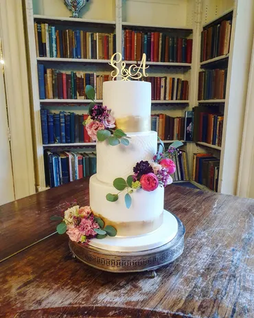 Two-tier white wedding cake with blue watercolour brushstroke detail on a coastal clifftop tablescape with candles
