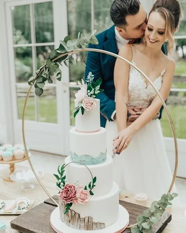 Four-tier white wedding cake with cascading mint green sugar roses on a pink cake stand