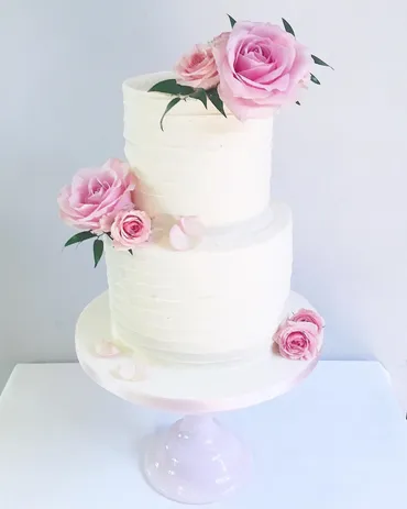 Four-tier white and blush wedding cake with lace detail, pearl swags and blush petal ruffle bottom tier