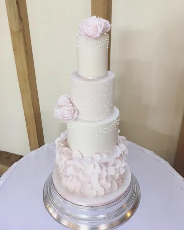 Two-tier white textured buttercream wedding cake with large fresh pink roses on a pink cake stand