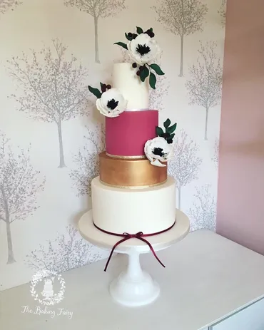 Four-tier white wedding cake with gold hoop, hand-painted flowers and Mr & Mrs Meads gold topper on a vintage table with candles