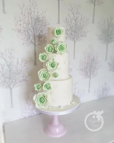 Bride and groom cutting a four-tier white wedding cake with sage green tier, pink roses and eucalyptus in a gold hoop arch