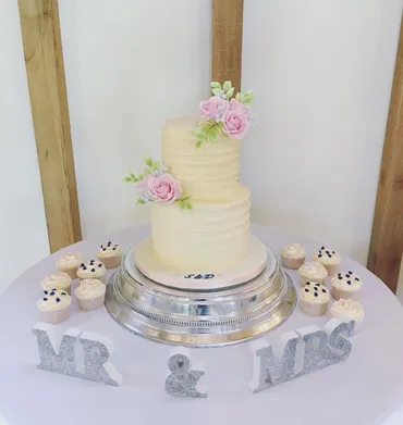 Four-tier semi-naked wedding cake with peach roses and Mr & Mrs Greaves wooden topper on a silver stand with fairy lights