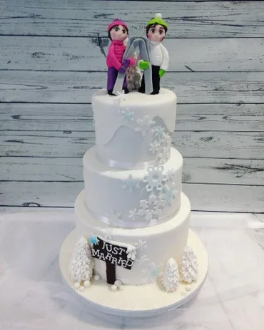 Three-tier white wedding cake with snowflake detail, Just Married sign and skiing couple figurine topper