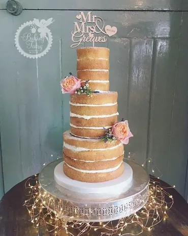 Two-tier ivory textured wedding cake with blush pink roses and S&D monogram on a silver stand with Mr & Mrs letters and cupcakes