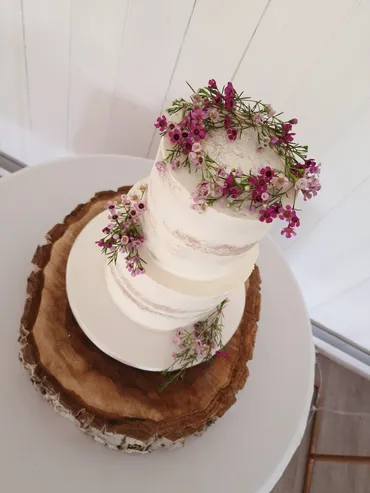 Three-tier semi-naked wedding cake with pink wax flowers on a wooden slice
