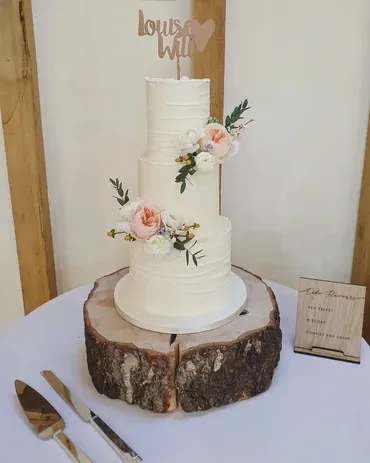 Four-tier white wedding cake with peach garden roses on a wooden log stand