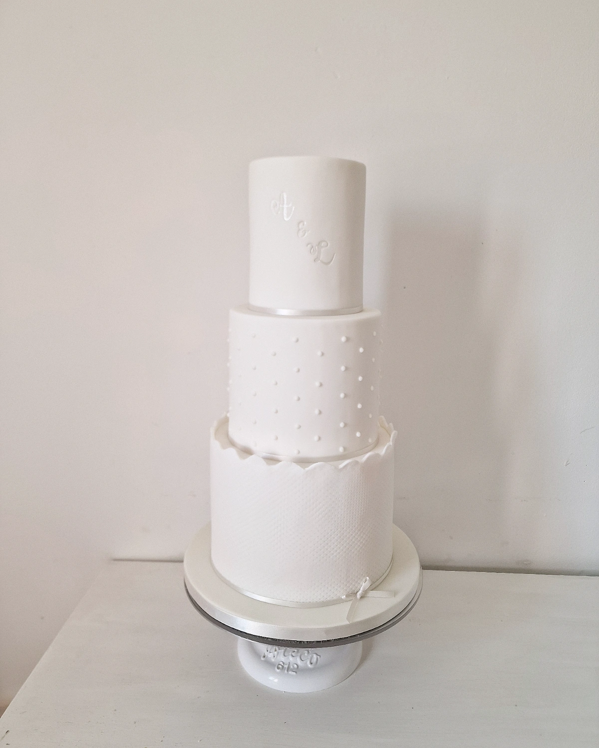 Three-tier all-white wedding cake with polka dot and lace texture detail
