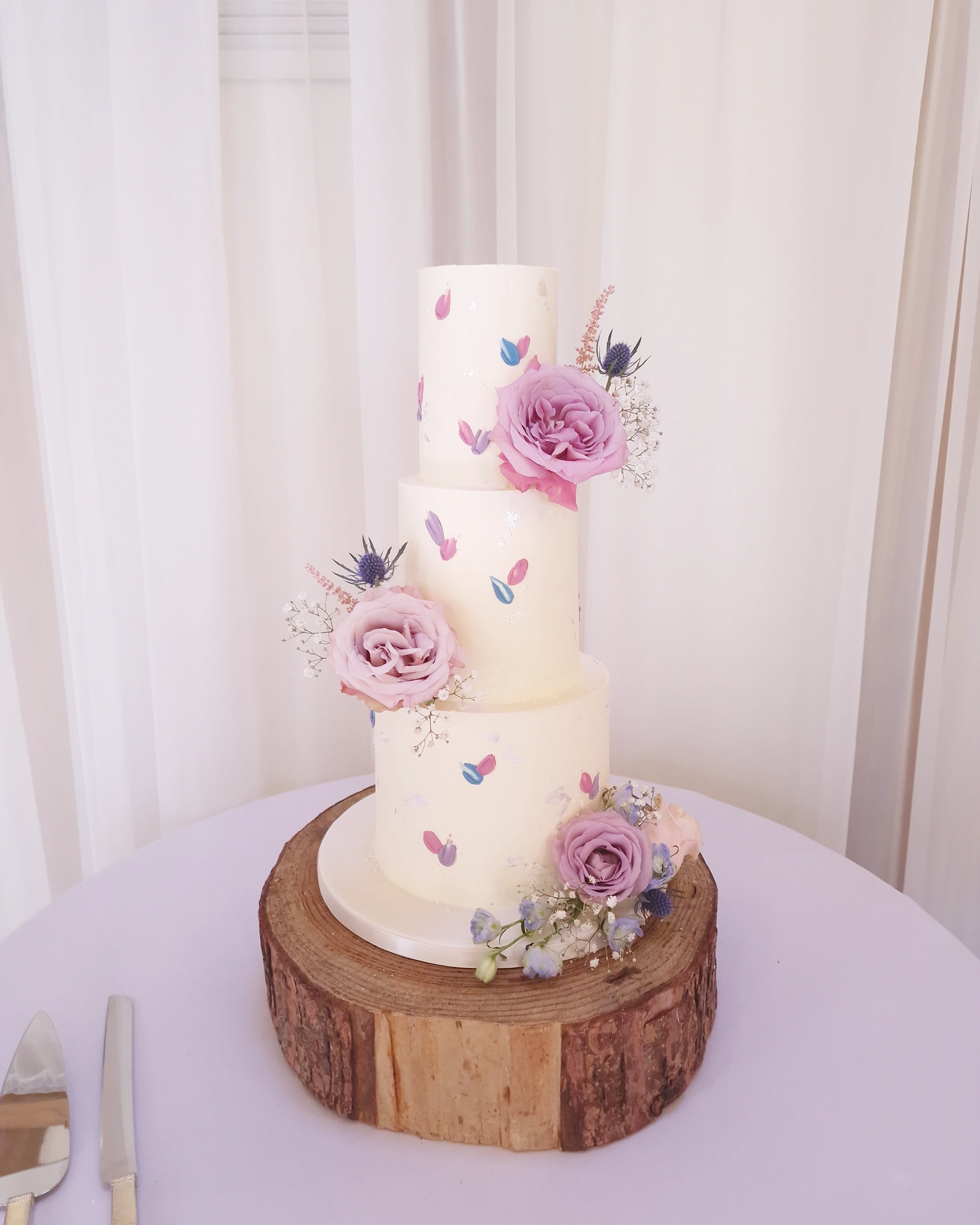 Four-tier white wedding cake with fresh pink roses on a wooden log stand