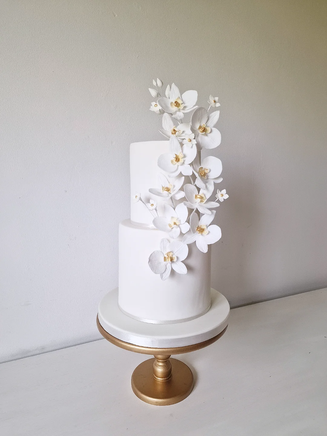 Two-tier white wedding cake with cascading sugar orchids on a gold stand