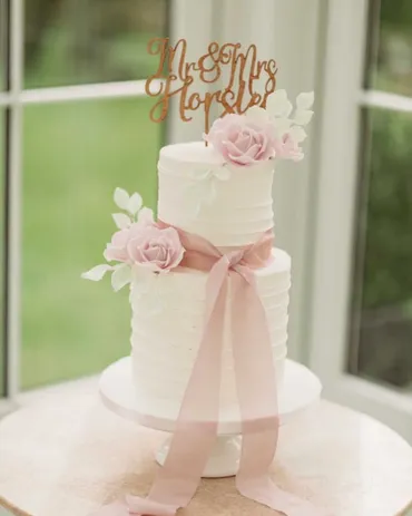Two-tier white textured wedding cake with blush pink roses and Mr & Mrs Horsler cake topper